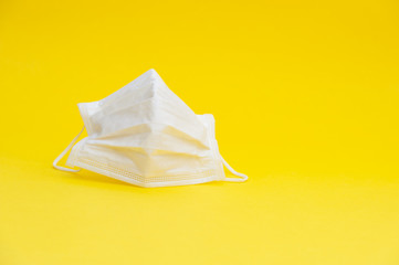 White surgical mask for protection against Coronavirus COVID-19 (SARS-CoV-2) and other contagious diseases. Copy space. Horizontal shot. Isolated on yellow background.