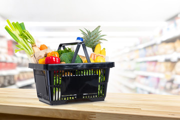 Shopping basket full of groceries on wood counter in supermarket background
