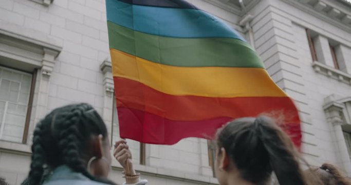 Women with LGBT rainbow colored flag at street parade.  Group of people in gay pride parade.

