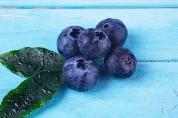 A few blueberries on a blue wooden background with a green leaf