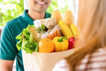 Smiling delivery man giving grocery bag to woman customer at home for online food shopping service...