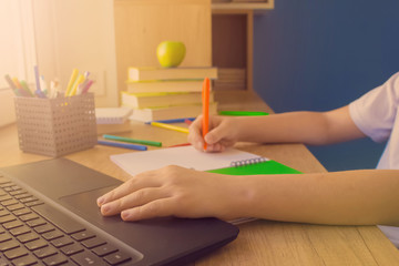 No face shot of a child boy typing on the keyboard of his laptop computer while doing homework, studying online at home at wooden table near the window