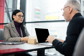 selective focus of smiling asian businesswoman talking with businessman in cafe