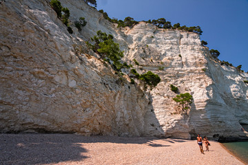Two bathers stroll on the white cliffs overlooking the Gargano sea in Puglia, Italy.