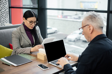 businessman using laptop and asian businesswoman using digital tablet in cafe