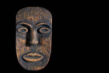 Fototapeta na wymiar African mask carved from wood on a black background. Free space, black background
