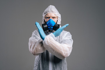 Fototapeta na wymiar Medical worker in hazmat suit, goggles and respirator is showing STOP gesture with two crossed hands. Concept of Coronavirus COVID-19 Pandemic. Studio shot in on isolated dark background