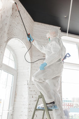 Coronavirus Pandemic. A disinfector in a protective suit and mask sprays disinfectants in house or...