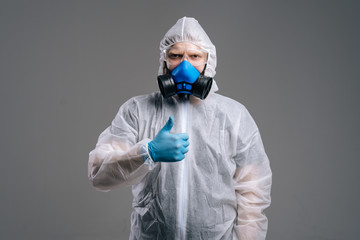 Serious epidemiologist in protective suit, goggles and respirator is showing thumbs up gesture. Concept of Coronavirus COVID-19 Pandemic. Studio shot on isolated background.