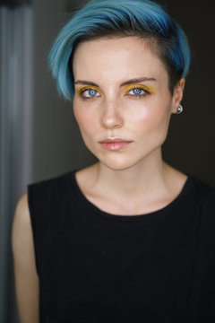 Portrait af a girl with blue hair and yellow eye makeup in a beauty salon in front of a ring light. Vertical shot.