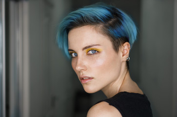 Portrait af a girl with blue hair and yellow eye makeup in a beauty salon in front of a ring light...