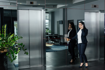 Smiling Asian businesswoman pushing button of elevator and talking on smartphone