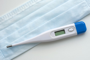 Thermometer on a medical mask in blue on a white background. Coronavirus Precautions Mask Protection.