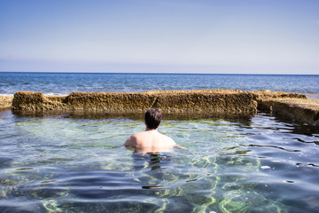 Young man enjoying a natural swimmingpool from sea water, enjoying open water space and warm calm water. with sea view