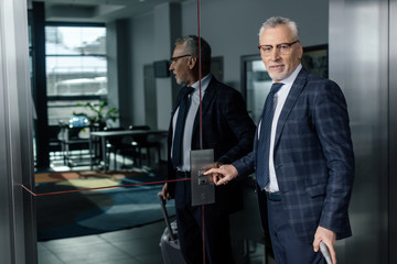 Smiling businessman pushing the button of elevator and looking at camera