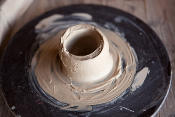 Potter's wheel with clay. Women's hands make a vase of clay.