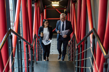high angle view of smiling businessman and asian businesswoman talking and walking on stairs