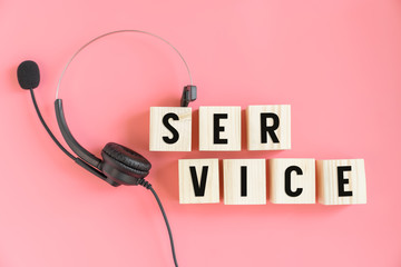 VOIP headset and wood block with text service on pink background. Communication support.