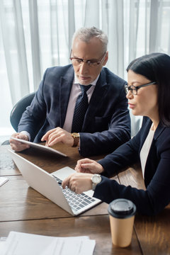 Businessman And Asian Businesswoman Looking At Laptop And Talking During Business Meeting