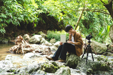 Asian man traveler photographer are taking photo and use laptop at beautiful forest. Travel...