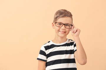 Cute little boy with eyeglasses on color background