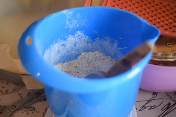 Blue bowl with flour and wooden spoon on the table in the kitchen close up