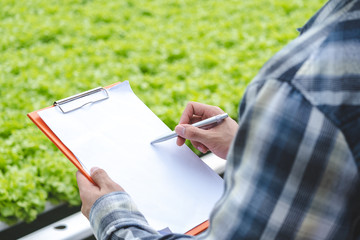 Closeup shot of farmer checking list in her clipboard about vegetable in hydroponic farm. The...