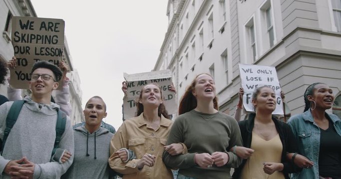 Group of activists holding hands and marching in a climate strike protest. Group of men and women protesting on climate change.
