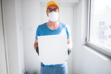 Fototapeta na wymiar Deliveryman with protective medical mask holding pizza box - days of viruses and pandemic, food delivery to your home and safety hygiene measures.
