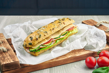 Sandwich in a ciabatta bun with chicken, tomatoes, cucumber, cheese and lettuce on a wooden tray....