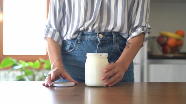 Woman's hand opening preserving jar with yoghurt