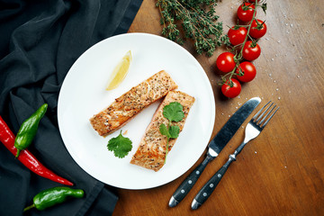 Serving appetizing salmon steak on a white plate in a composition with a black cloth and ingredients on a wooden table. Grilled seafood