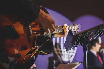 Concert view of an electric guitar player with vocalist and musical jazz band orchestra performing...