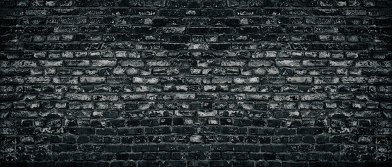 Old black shabby brick wall wide texture. Aged dark brickwork with peeling paint. Gloomy grungy widescreen background