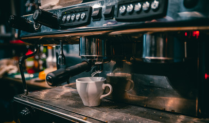 coffee machine is pourig coffee to white cup in bar