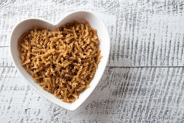 Wholegrain spelt fusilli on plate on white wooden background.