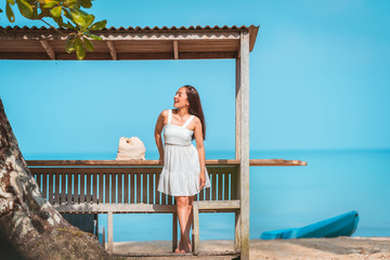 asian girl in white dress by posing relax in bench wood on the beach with sunlight shine