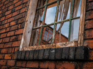 Broken window, looking through frame to other window frame. Red brick work. Faded and obsolete. 