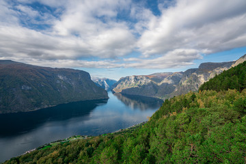 Fjords of Aurland in Norway, on a sunny day in early autumn. Clouds and sky reflect in the water.