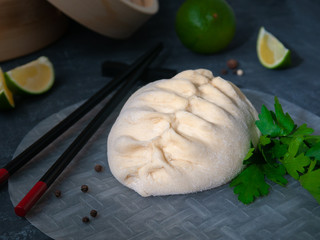 Pyans bun steamed. Filled with chicken, carrots and cabbage. In the background are a bamboo double boiler, lime, chili pepper and soy sauce. View from above.