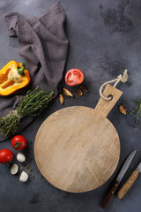 Italian cuisine. Wooden board with mozzarella, yellow pepper, tomatoes and thyme on a grey background. Knife, fresh vegetables and spices on the background. Rustic. Background image, copy space