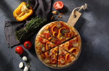 Italian cuisine. Pizza with mozzarella, yellow peppers, tomatoes and thyme on a wooden board on a grey background. Vegetable pizza.  Rustic. Background image, copy space