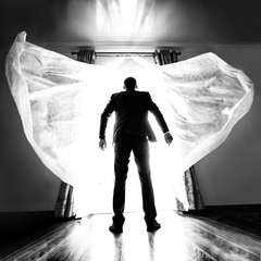 A man in a business suit in front of a bright light . Artistic overexposure of a man on the threshold of a new .Black and white photo of a man from the back in front of a very bright light
