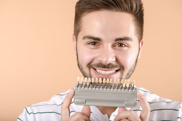 Young man with teeth color samples on beige background