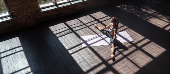 Relaxed sexy fit young woman wear sportswear stretch sit legs split on wooden floor mat in sunny...