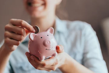 Fotobehang female hands hold a pink piggy bank and puts a coin there. The concept of saving money or savings, investment © Nana_studio