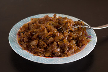 Close up caramelized onion on plate with fork on the black background