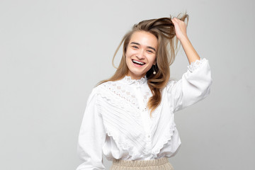 Fototapeta premium Very emotional woman laughs while tearing her stomach. Portrait of a beautiful woman on a white-gray background