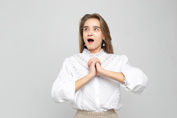 Surprised young woman screaming on a white-gray background. Watch camera. Beautiful mixed race businesswoman open mouth and close palms