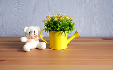 A beautiful soft toy and a watering can with flowers on a wooden table. Bear beige